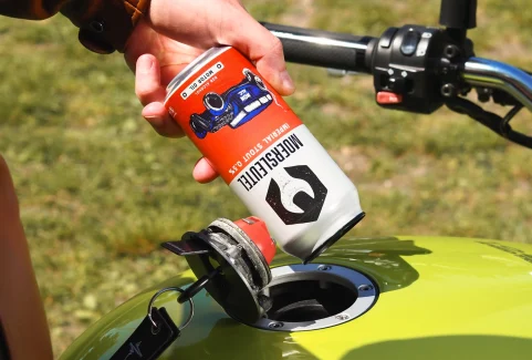 Personne s'amusant à verser de la bière Moersleutel Motor Oil Non-Alcoholic Stout dans le réservoir d'une moto.